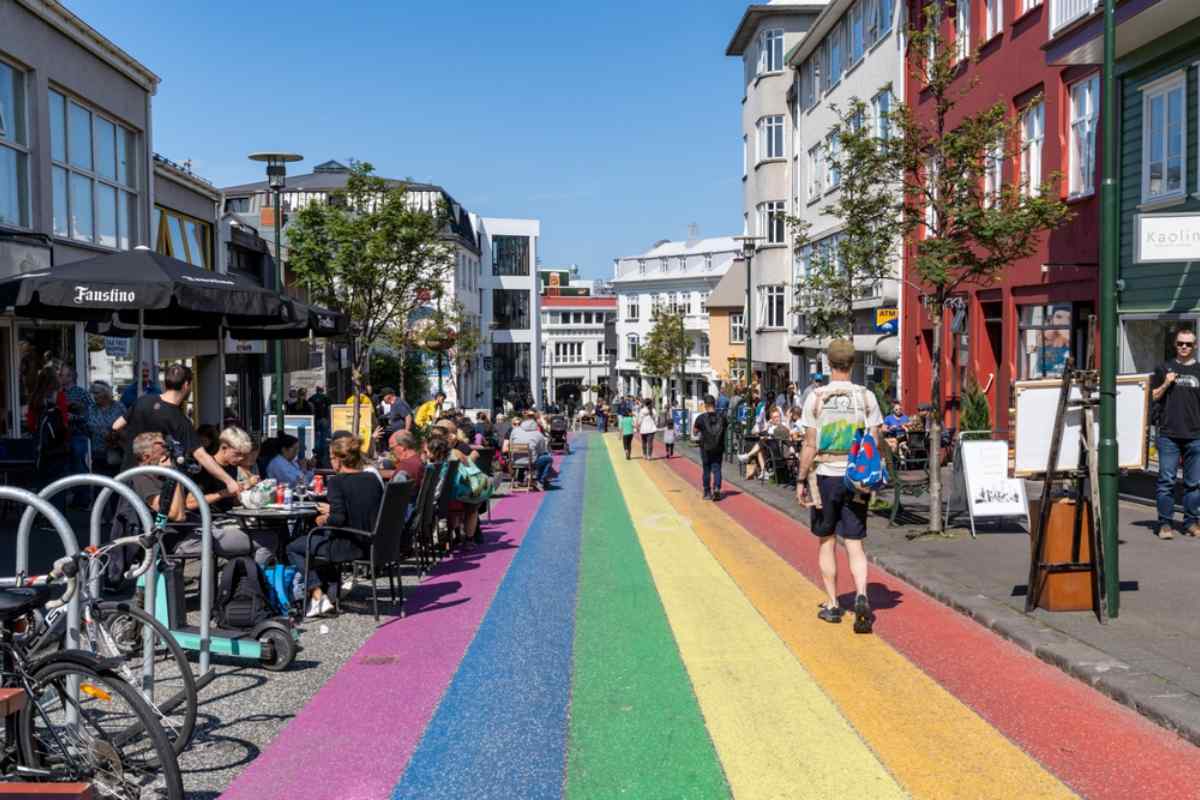 Rue pi&eacute;tonne peinte aux couleurs de l&rsquo;arc-en-ciel dans le centre de Reykjav&iacute;k avec des caf&eacute;s en terrasse anim&eacute;s.