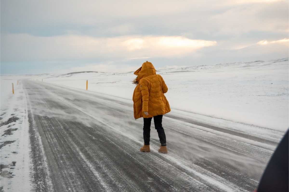 Assurance couvrant les dommages liés au vent en Islande Touriste en veste jaune essayant de marcher sur une route très venteuse en Islande