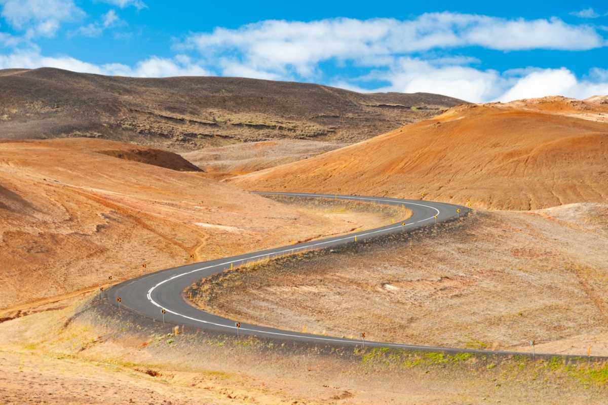 La Ring Road d'Islanda Strada vuota e tortuosa che attraversa colline vulcaniche colorate in Islanda con pendii arancioni e marroni su entrambi i lati