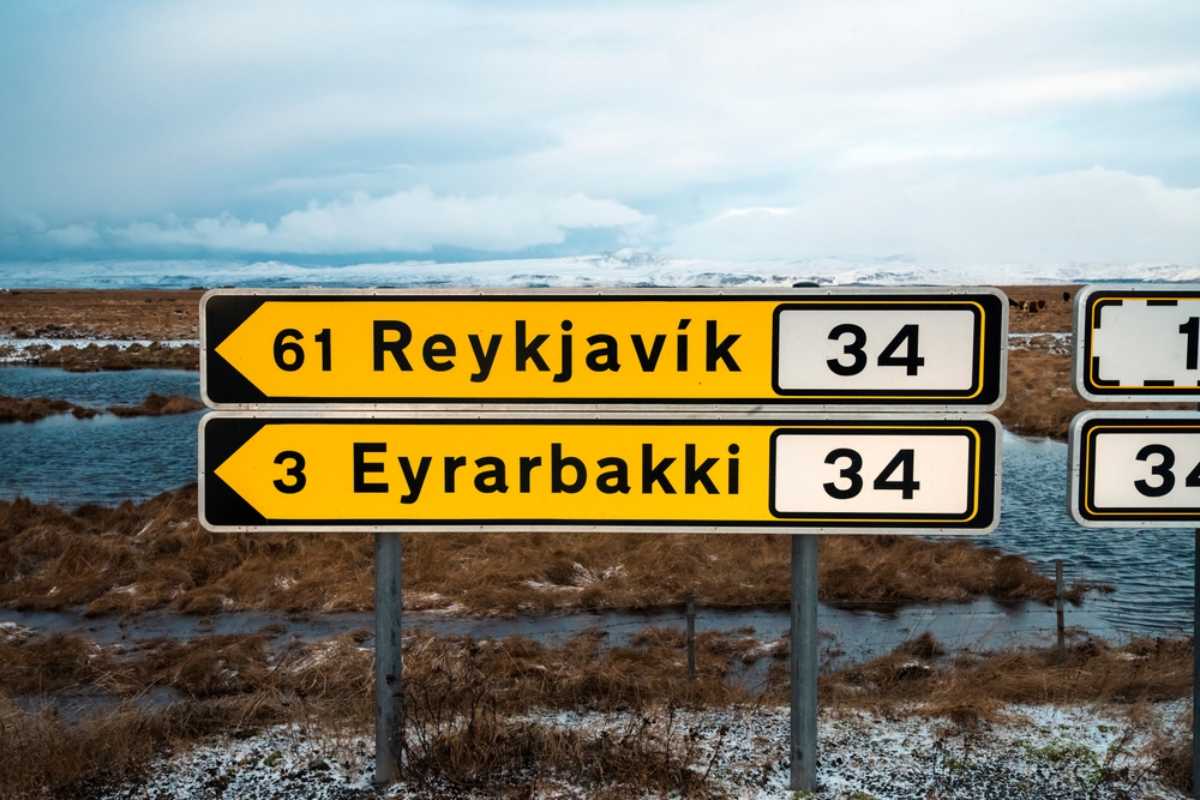 Strade rurali in Islanda Cartelli stradali gialli in Islanda che indicano Reykjavík e Eyrarbakki accanto a zone umide e montagne innevate sullo sfondo