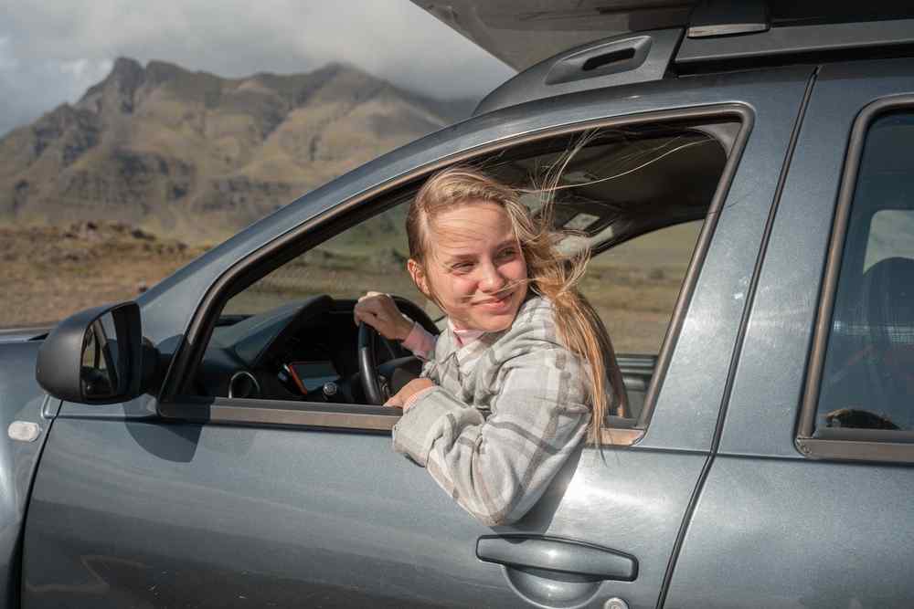 Viaggiatrice affacciata al finestrino di un&rsquo;auto a noleggio in un paesaggio islandese ventoso.