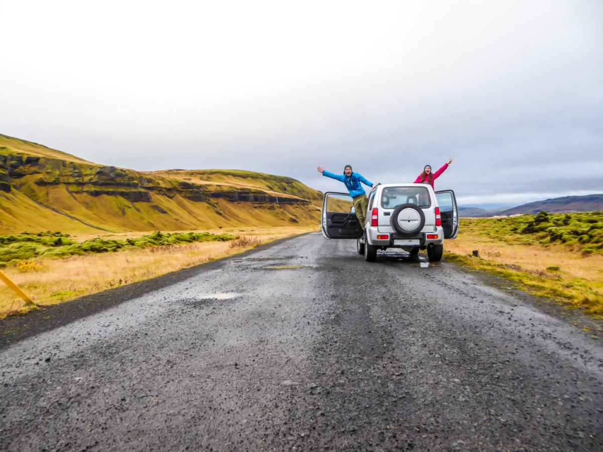 Stare al sicuro sulla strada mentre si guida in Islanda Coppia felice che allunga le mani fuori dalla loro auto 4x4 in mezzo a una strada deserta